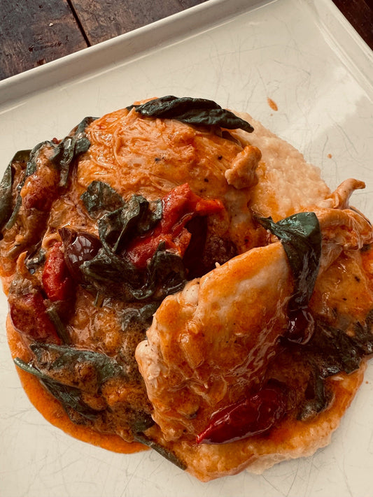photo of chicken thighs with sauce, spinach on a white square plate.